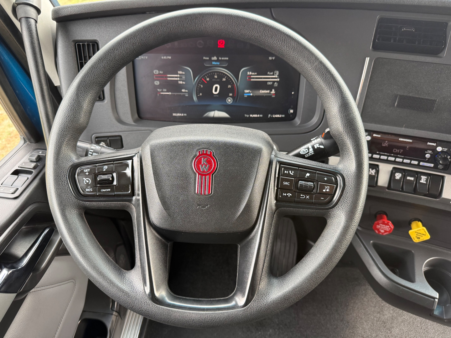 Kenworth T680 interior steering wheel and dashboard with digital gauge cluster, steering wheel controls, and center console including red and yellow caution caps.
