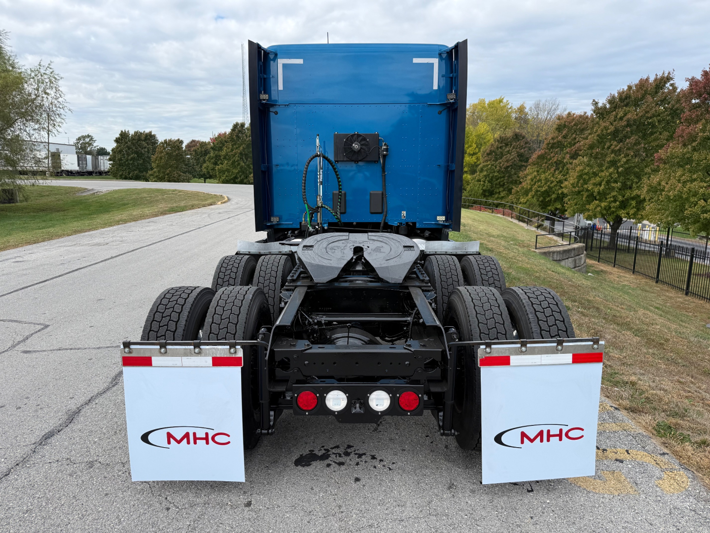 Blue Kenworth T680 rear view showing dual rear axles, fifth-wheel, mud flaps with MHC logos, and trailer kingpins. VIN and stock not visible in image.