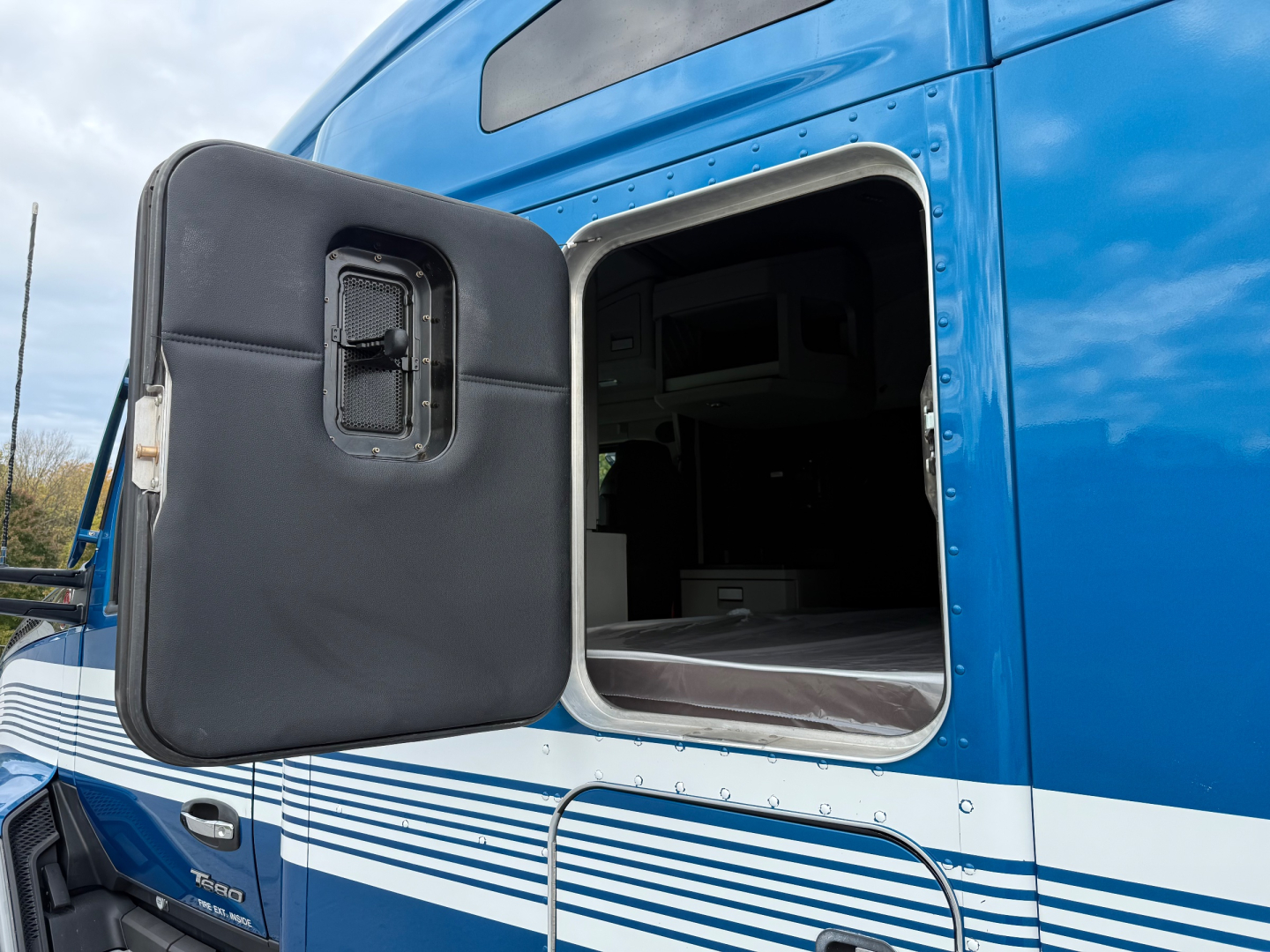Kenworth T680 sleeper truck door open showing side fuel door and interior cab access panel.