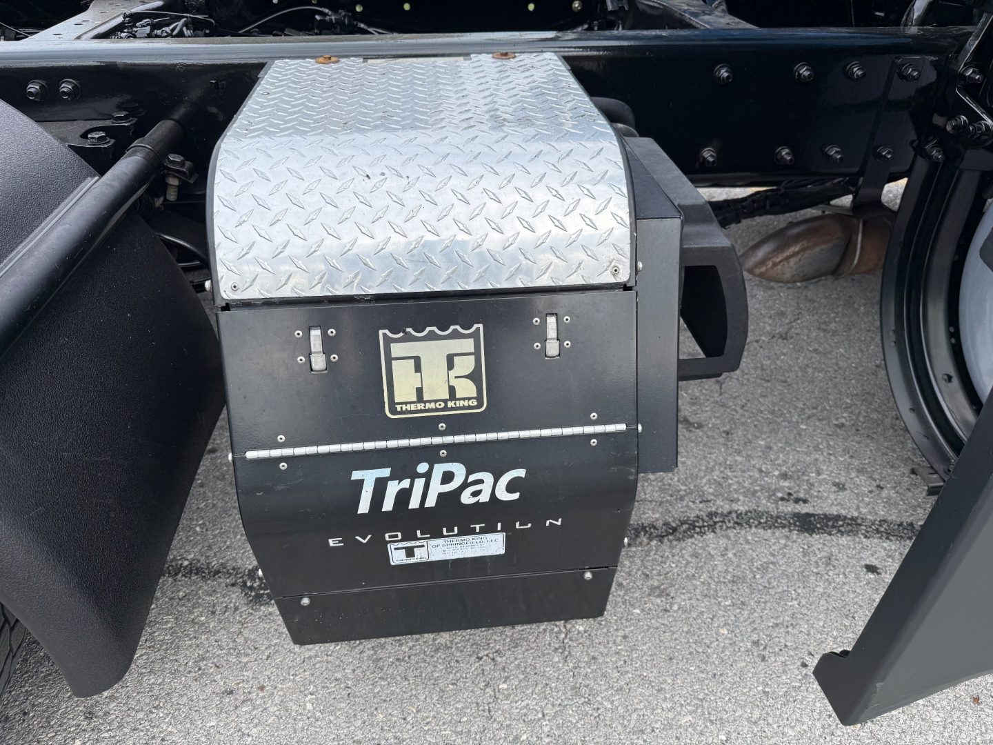 TriPac Evolution battery/auxiliary system under a 2023 Kenworth T680, black housing with Diamond plate top, TriPac Evolution branding, fuel/electrical compartment visible.