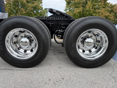 Kenworth truck axle with two Bridgestone tires and polished chrome wheels, chassis frame visible between wheels.