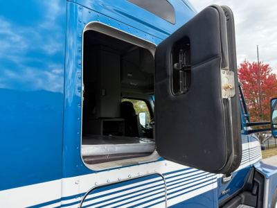 Truck cab door open on a blue Kenworth T680 side view showing sleeper cab interior and door with black panel.