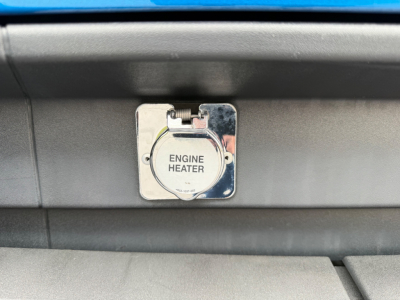 Kenworth truck engine bay area showing a metal engine heater access panel with circular cap labeled ENGINE HEATER.