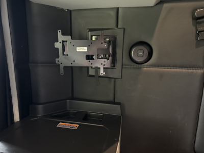Kenworth T680 interior area showing a mounted bracket and panel with a circular power outlet; storage pocket and a label area visible.