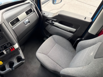 Cab interior of a 2023 Kenworth T680 semi-truck showing driver seat, dashboard, and center console with cup holders.