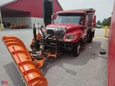 Dump truck with plow attachment in front of red building. 2015 International TerraStar dump truck showing large orange snow plow and chrome front grille.