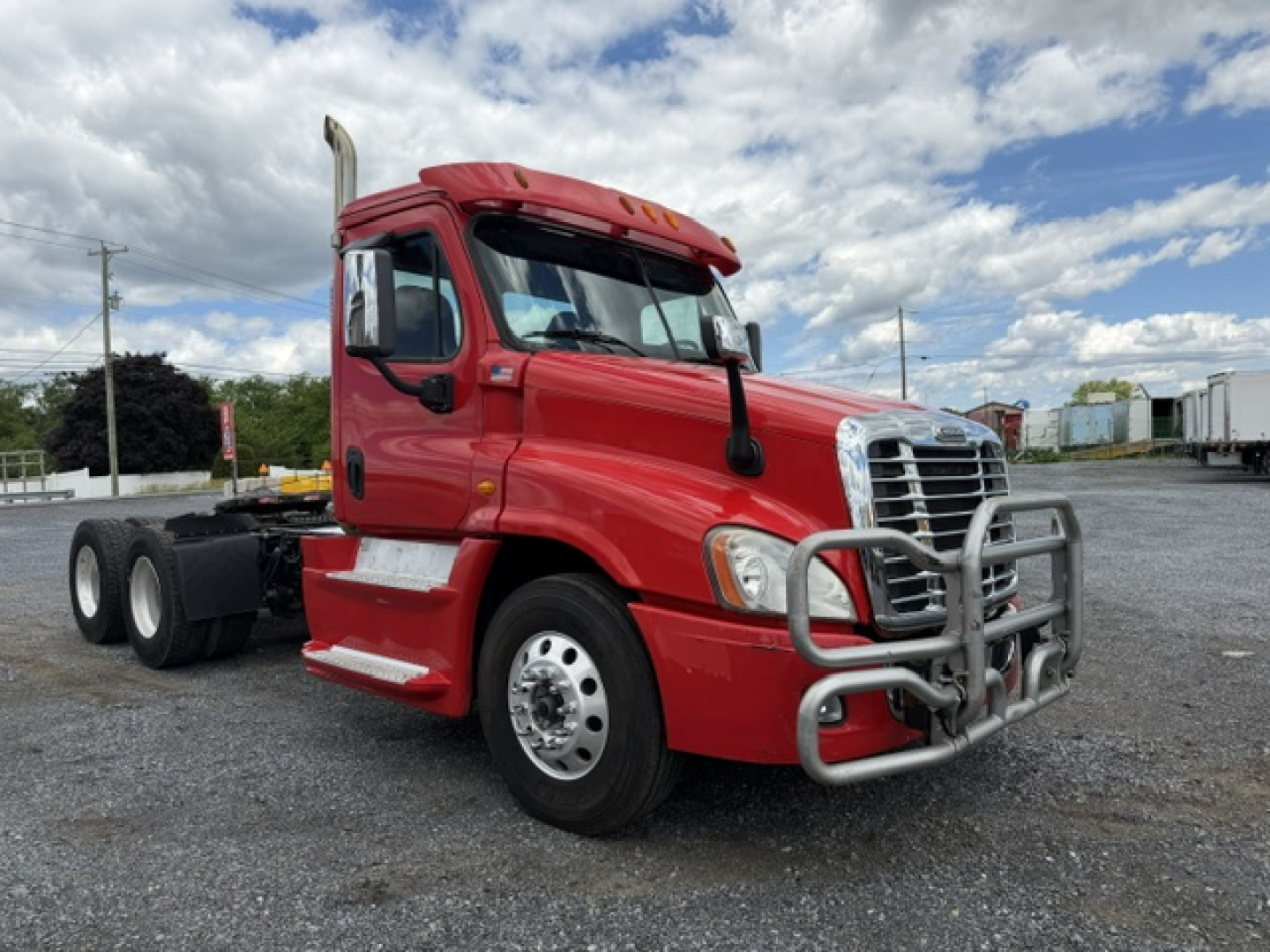 Red Freightliner Cascadia CA125DC truck cab showing front grille guard and chrome bumper with dual rear axles in background.