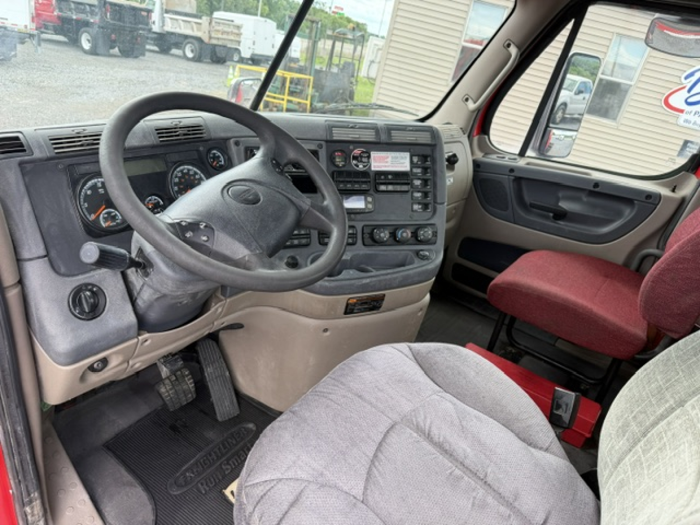 Freightliner Cascadia cab interior showing steering wheel, dashboard with gauges, center console, and driver seat.