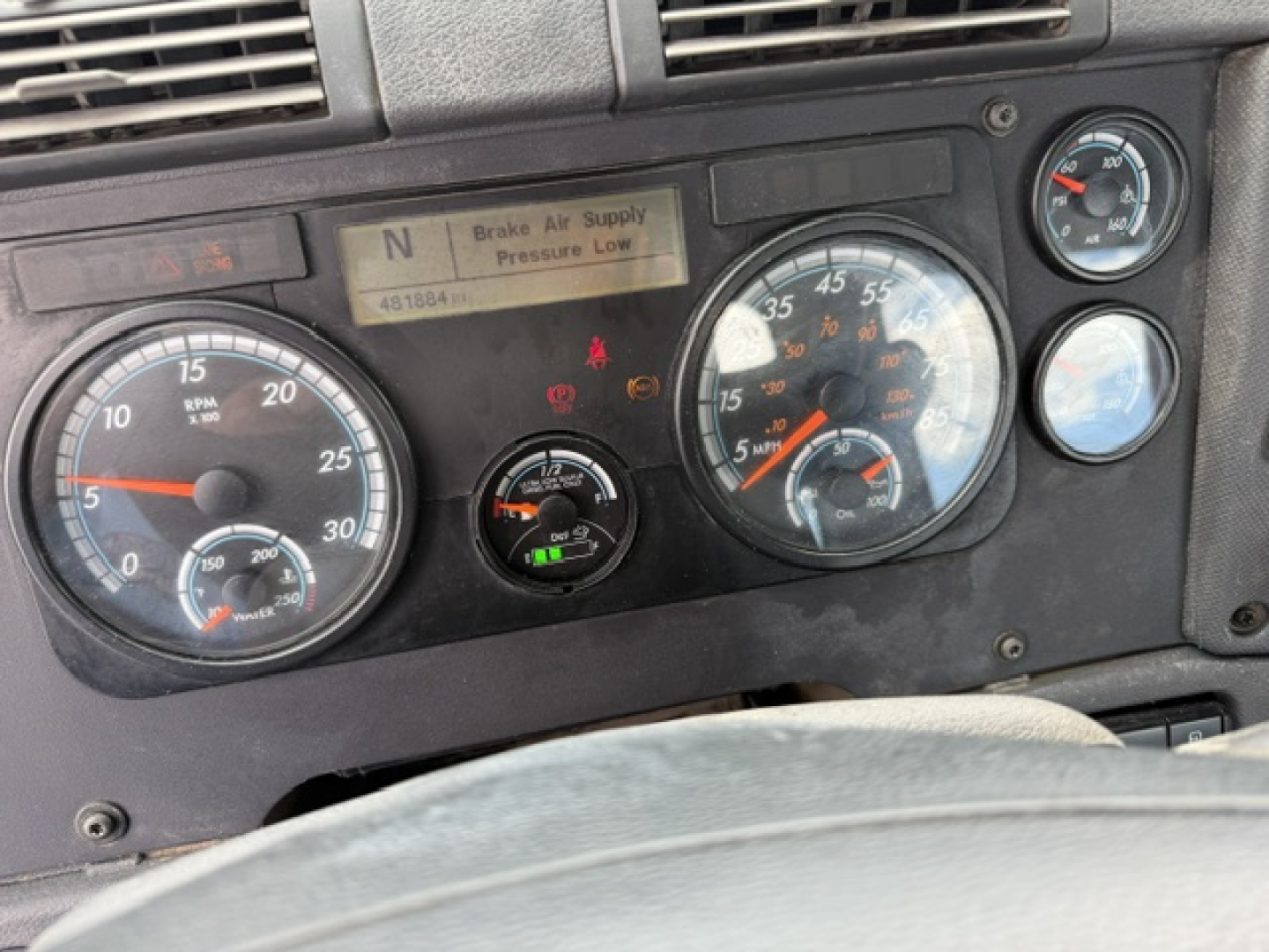 Dashboard of a Freightliner Cascadia shows instrument gauges and warning indicators. Visible text: 'Brake Air Supply Pressure Low' on center display, numbers on gauges, and small labels around. VIN not fully legible in image.