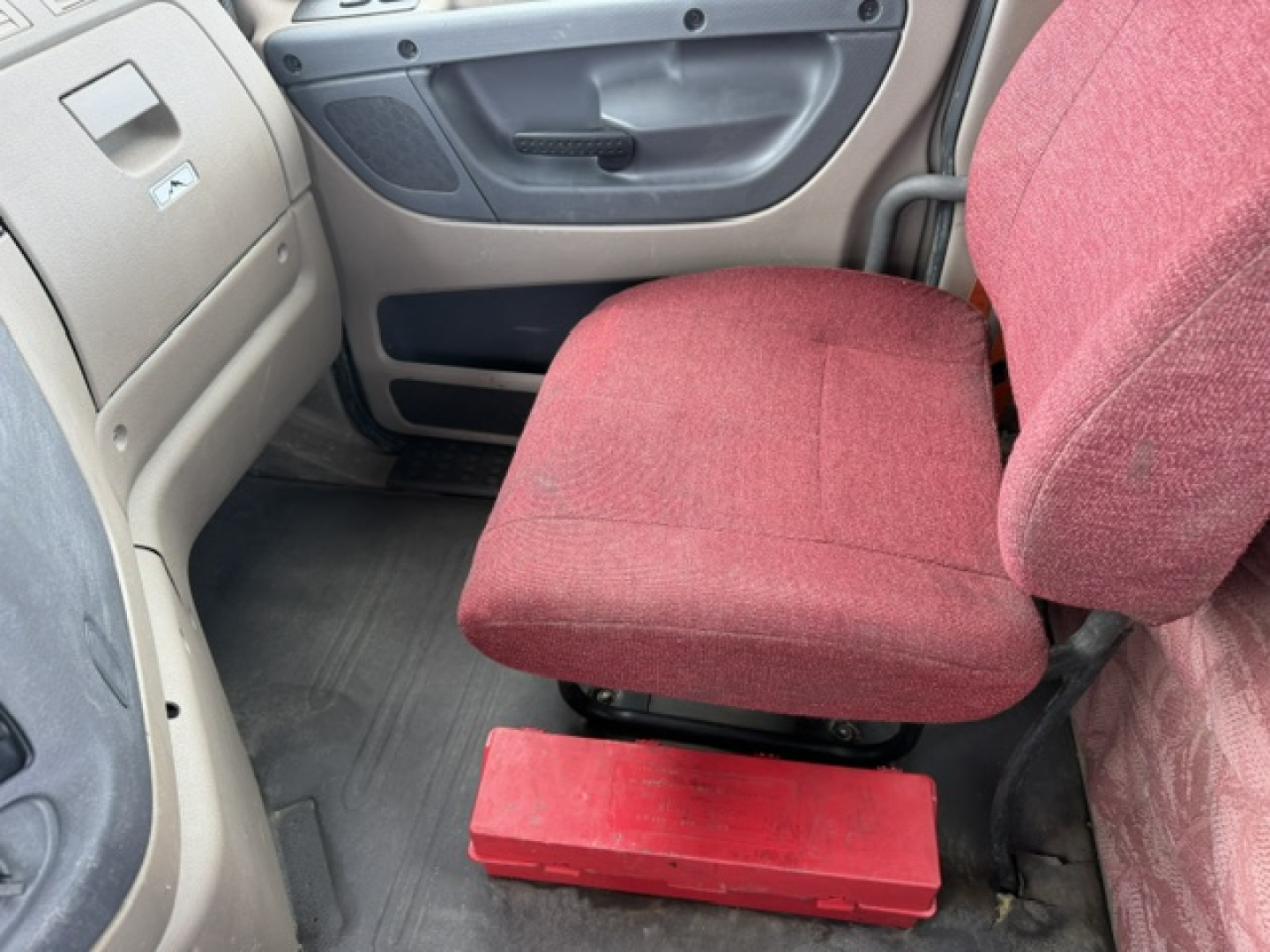Cab interior showing red vinyl driver seat and gray door panel in a Freightliner Cascadia truck.