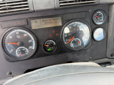 Dashboard of a Freightliner Cascadia shows instrument gauges and warning indicators. Visible text: 'Brake Air Supply Pressure Low' on center display, numbers on gauges, and small labels around. VIN not fully legible in image.