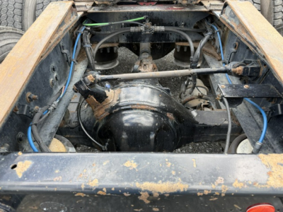 Freightliner Cascadia engine bay view showing drive axle and suspension components with blue and green hoses, wiring, and rugged frame.