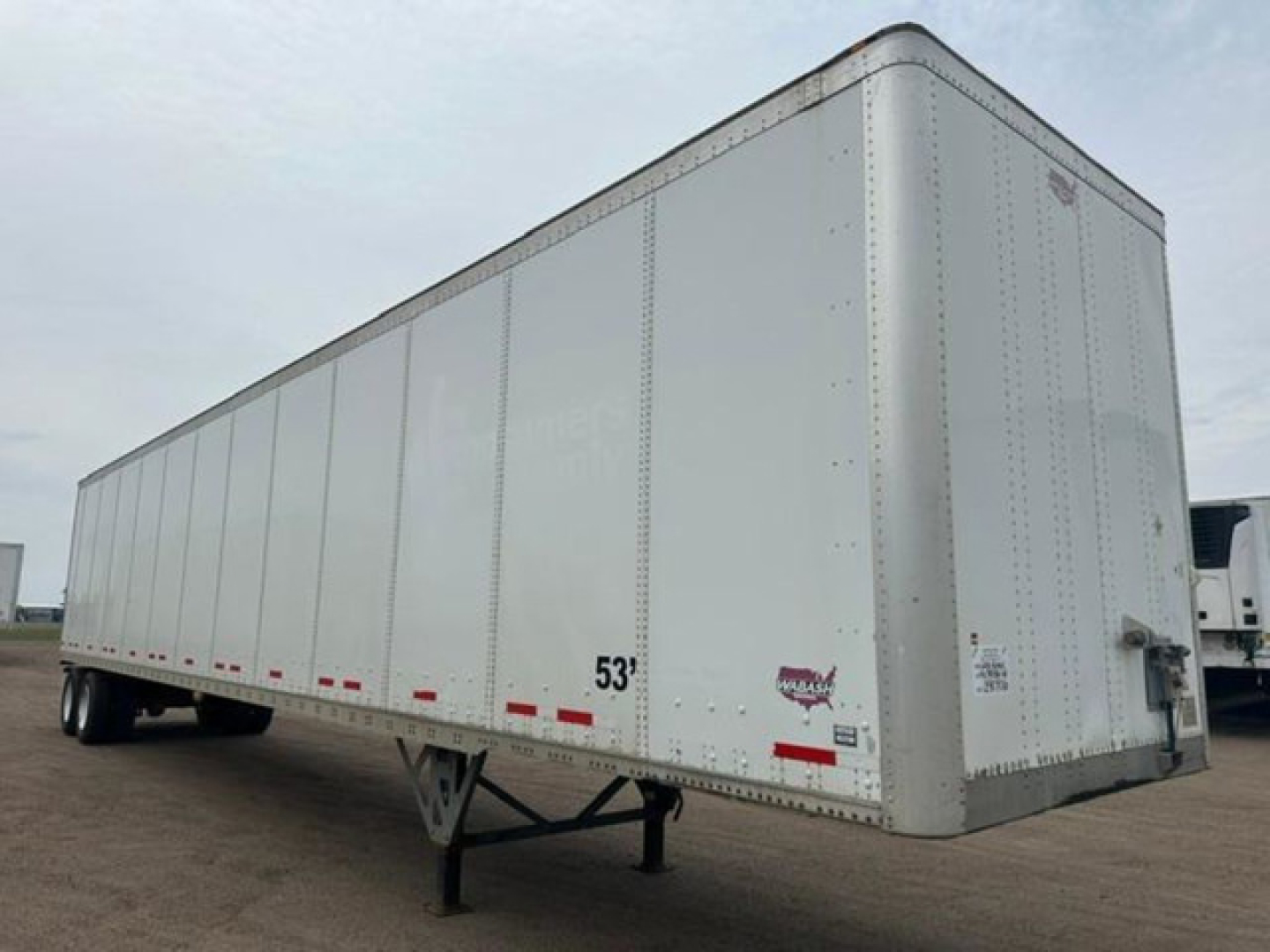Trailer side view showing white Wabash van trailer with 53' mark and riveted panels, undercarriage and tandem wheels visible.