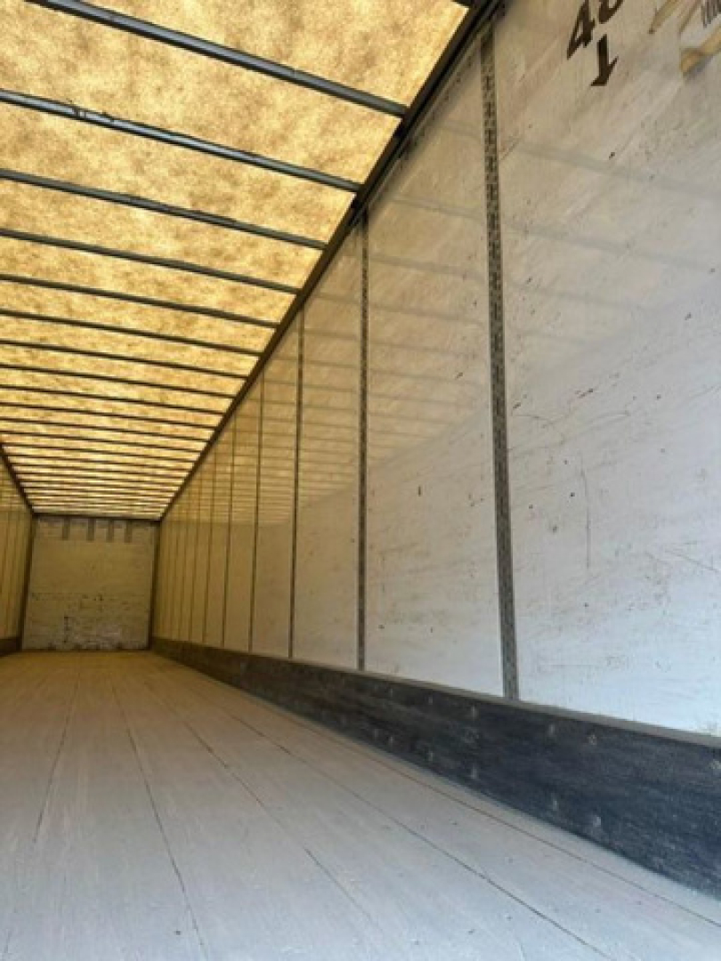 Trailer interior showing empty cargo space with white walls, wooden floor, and roof beams; no visible branding or text.