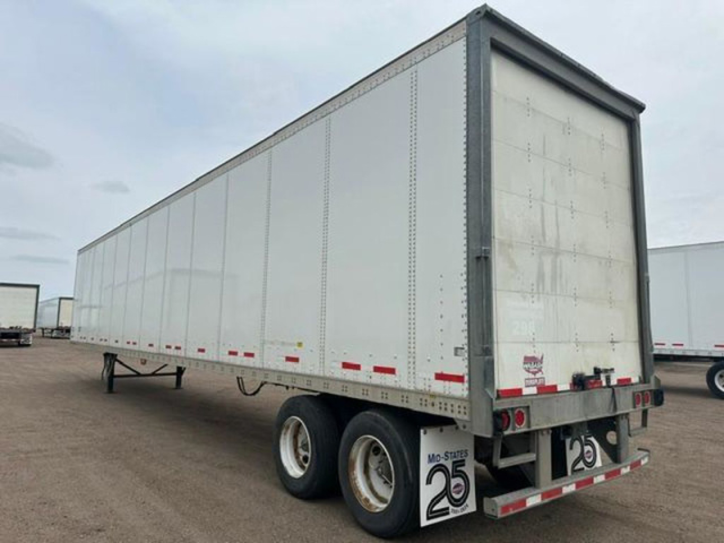 Trailer side view showing a white Wabash van trailer with swing-out rear doors, dual rear axles, and red/white reflective tape along the lower edge.