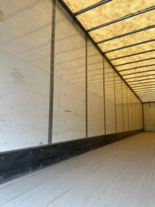 Trailer interior showing long white side walls with vertical posts and a wooden ceiling ridge, empty cargo area in a Wabash van trailer