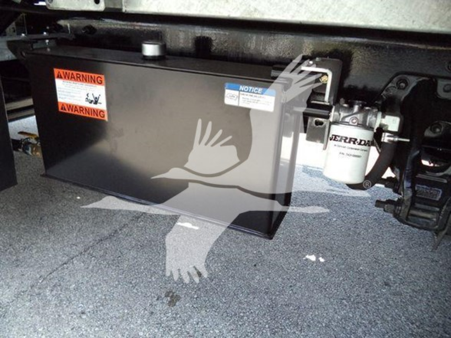 Kenworth T880 rollback undercarriage showing a black rectangular battery box with warning labels and a white cylindrical filter nearby.