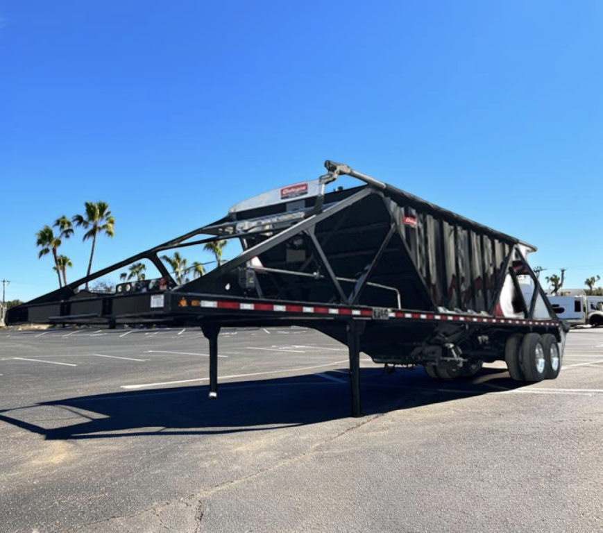 Trailer showing a GALLEGOS SAND HOPPER with a long black steel frame and dual rear axles, parked on a paved lot.