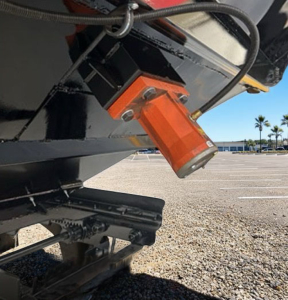 Trailer hitch area showing an orange lock pin and underside of a hopper trailer with black painted steel frame and hydraulic components.