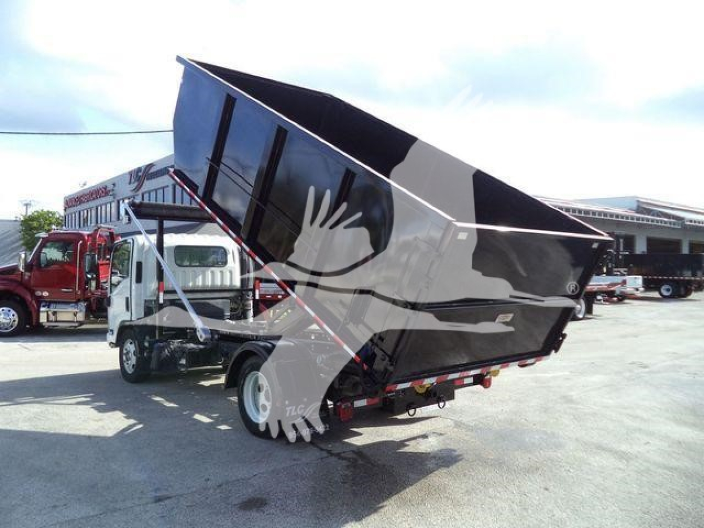 Isuzu NPR truck with a raised dump bed in a deployment lot showing side view of chassis and hydraulic mechanism.