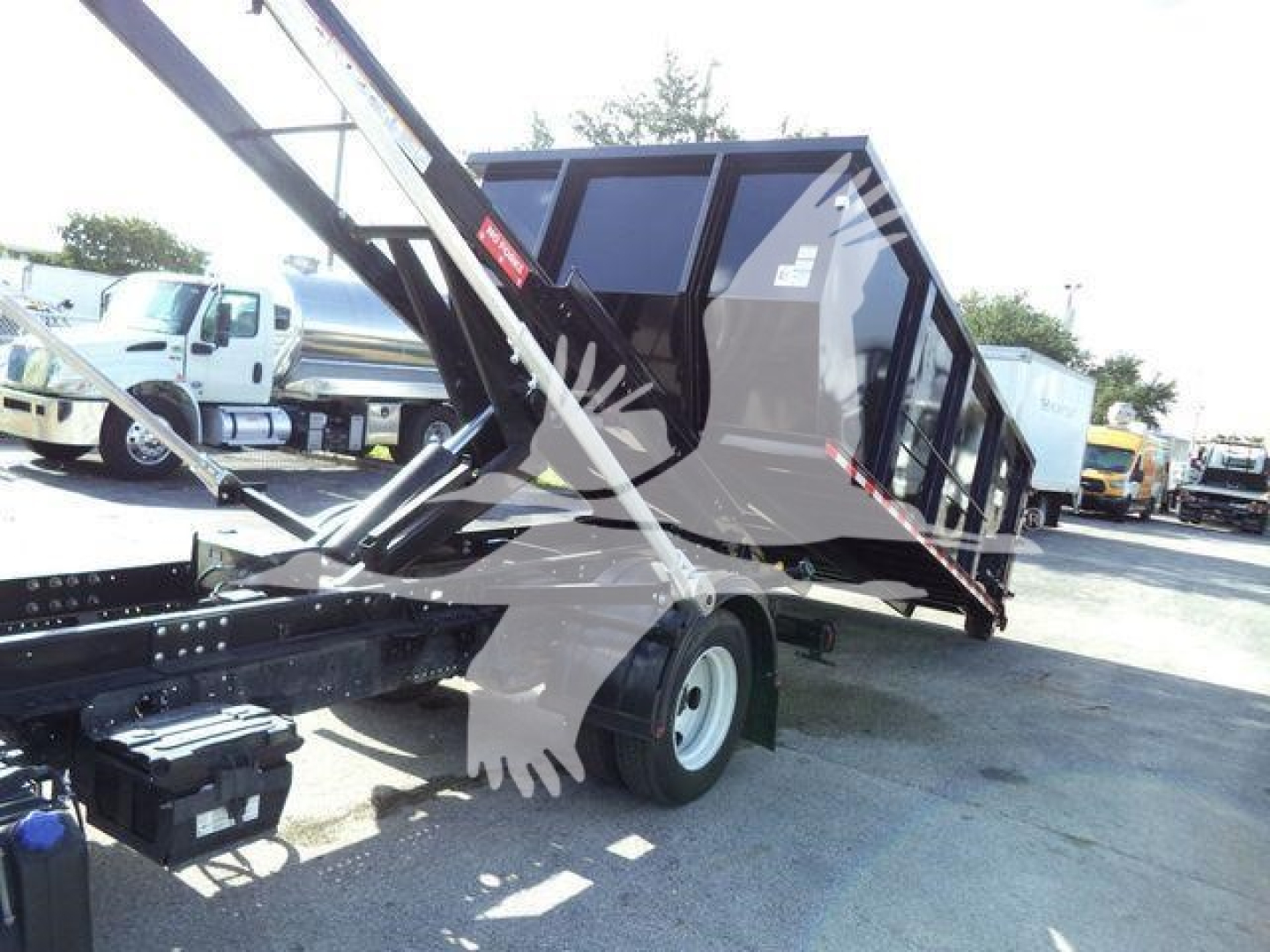 Isuzu NPRR truck with hydraulic dump bed in a rollover configuration showing rear wheels and bed side; no readable text visible.