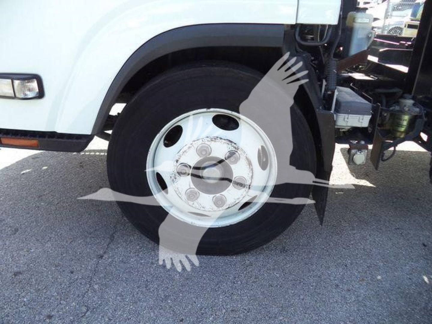 Isuzu NPR roll-off truck front wheel and fender visible, white cab, steel wheel with tire, visible part of chassis and side mirror.