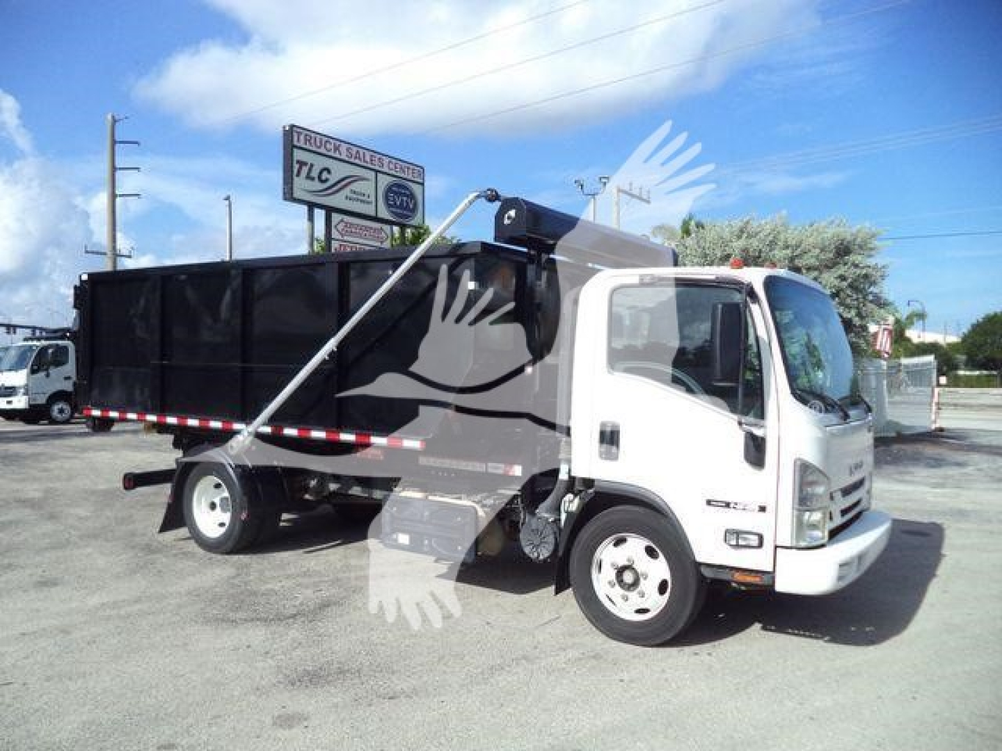 Isuzu NPR/NRR roll-off truck in-service showing cab and black dump body with hydraulic lift, side marker lights, front grille, and wheel wells.