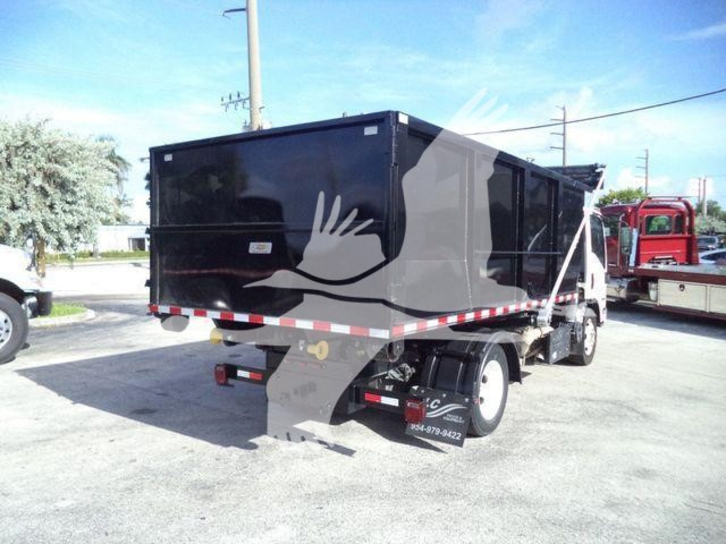 Isuzu NPRR roll-off truck rear/side showing black container and dual rear wheels with white cab edge visible