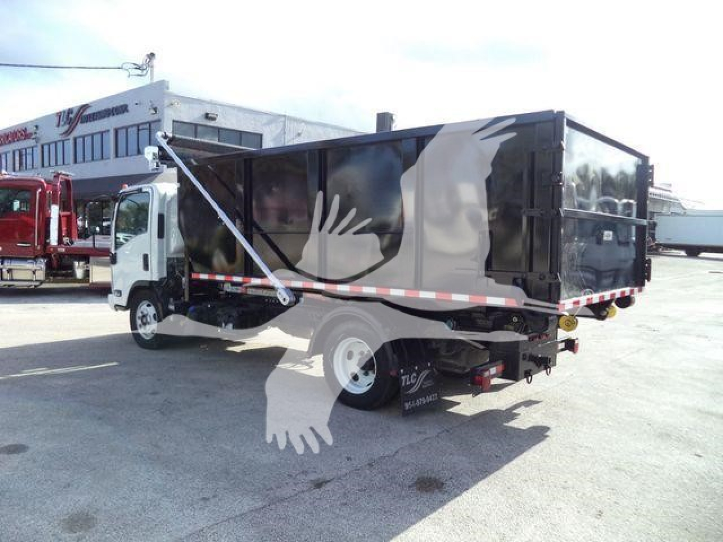 Isuzu NPRR roll-off truck showing side panel and rear, two-tone black dump body, white cab, reflective tape.