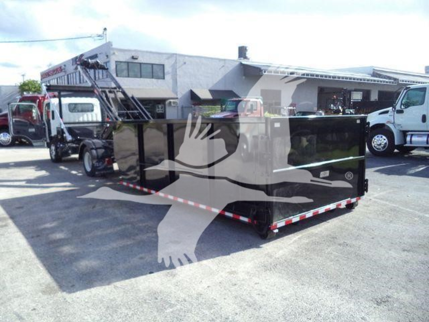 Isuzu NPRR roll-off truck bed in a rear three-quarter view showing a black steel dump/box with white safety stripes and storage compartments.