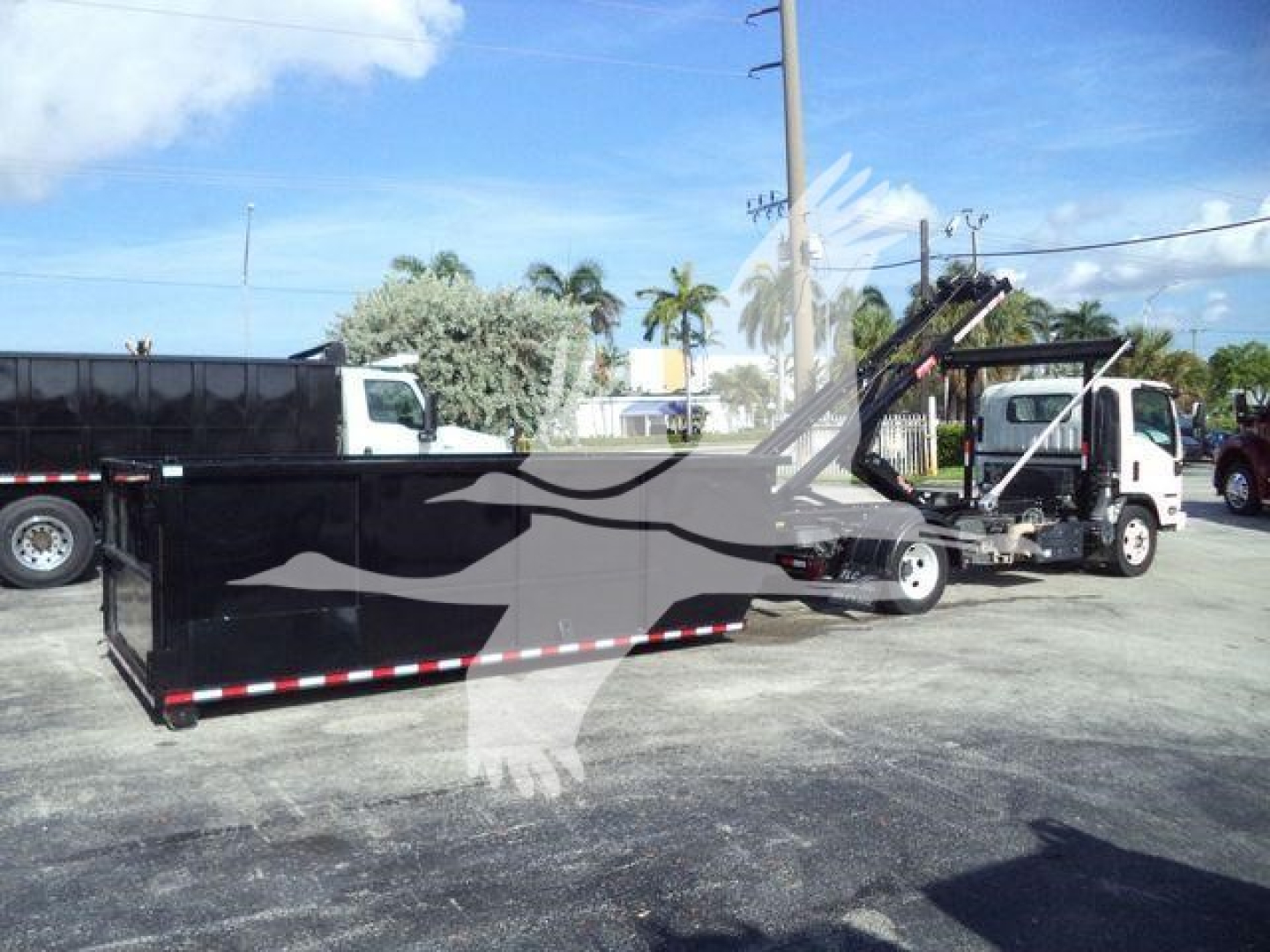 Isuzu NR-R rolloff truck with a long black trailer and a hooked loader, showing the side of the vehicle and equipment. No legible labels or text visible on the image itself.
