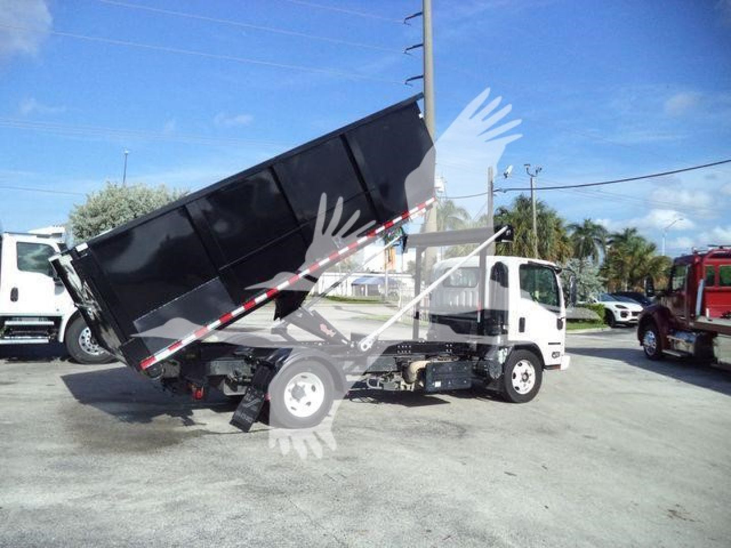 Isuzu NPR/NRR rolloff truck with dumping bed raised showing hydraulic cylinder and rear chassis components.