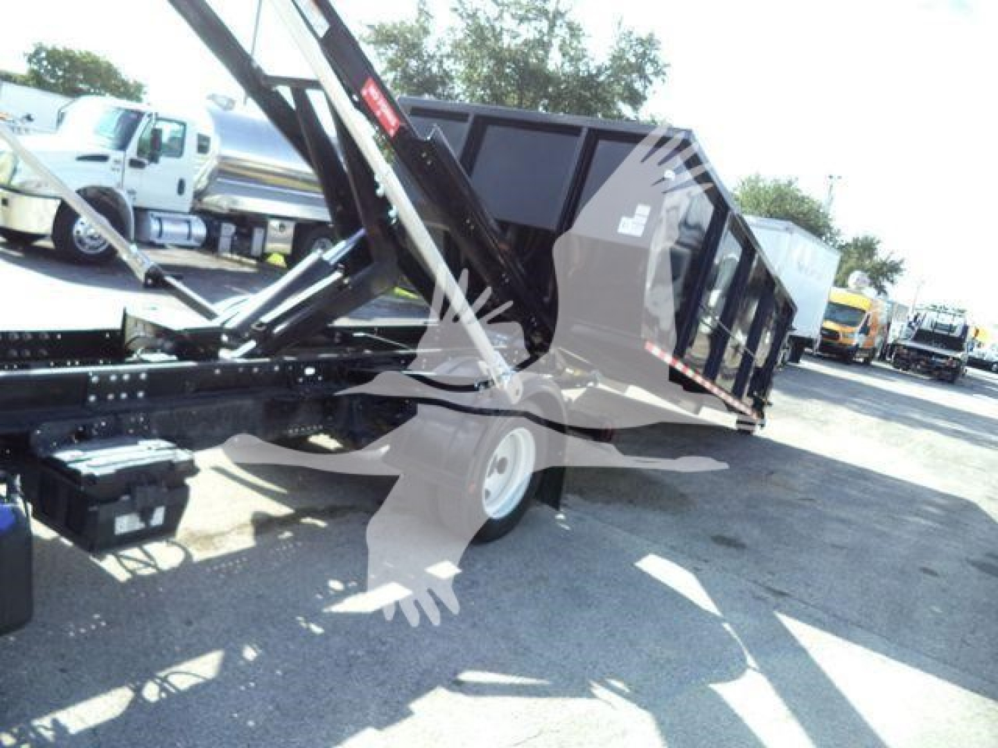 Isuzu NPRR/roll-off truck chassis with hydraulic dump bed and crane arm in operating position; side view shows black dump body and wheels.