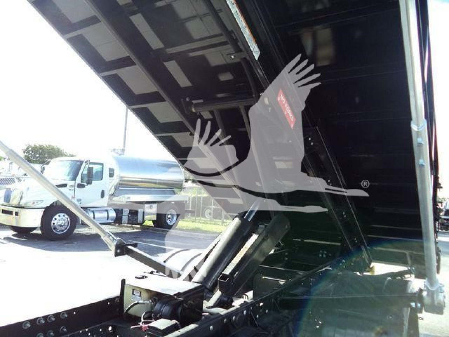 Isuzu NRR truck bed with hydraulic tilt, metal components, and a raised black bed panel. Visible text on stickers: none legible; general equipment area.