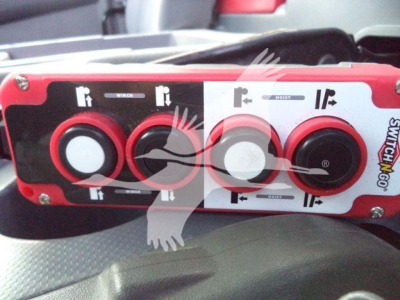 Isuzu NRR control panel with red/black switches and white labels in a roll-off truck, showing winder/motion controls.