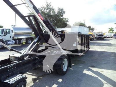 Isuzu NPRR roll-off truck bed with hydraulic arms and dumpster container visible; side view showing chassis and towing setup.