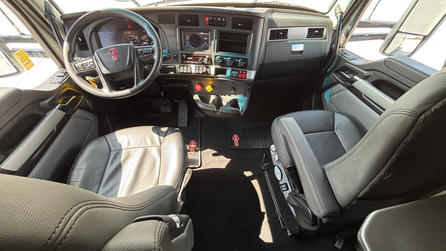 Kenworth T680 cab interior showing steering wheel with Kenworth logo, dash panels, center console, and seating.
