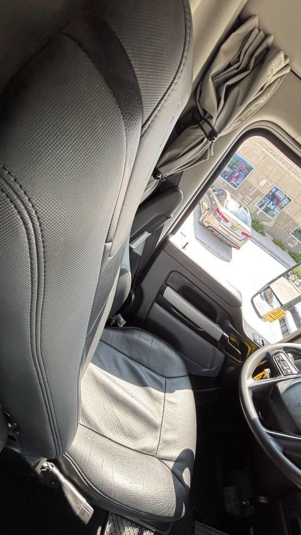 Interior of a 2023 Kenworth T680 cab showing steering wheel and driver's seat with seat belt; windows and dashboard visible.