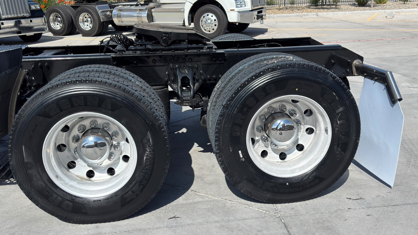 Kenworth T680 chassis view showing tandem rear wheels with chrome hubcaps and dual tires; black frame with mudflaps partially visible.
