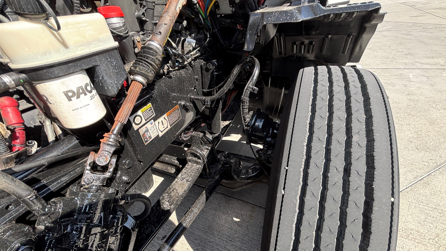 Kenworth truck engine bay/view showing hydraulic reservoir and exposed components with front tire in foreground.