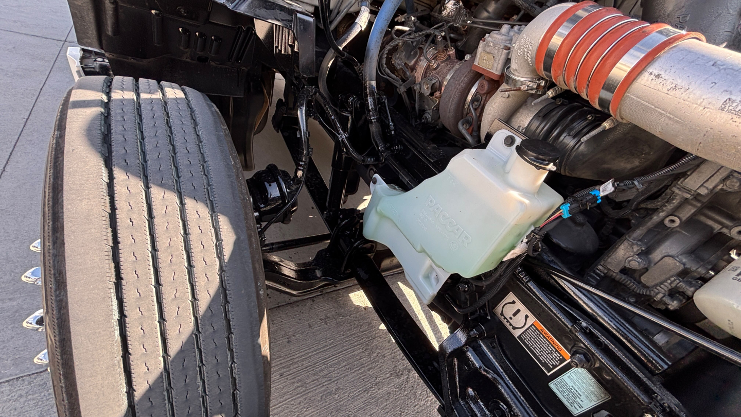 Kenworth T680 engine bay view showing coolant reservoir and intercooler piping with white/green translucent coolant bottle and metal lines.
