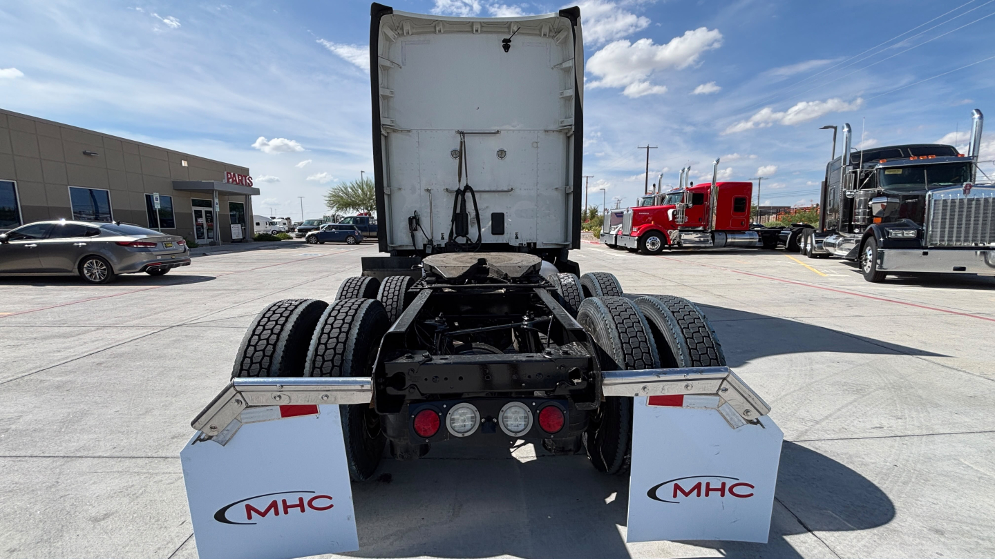 Kenworth T680 chassis rear view showing dual rear axles and trailer hookups, white MHC mud flaps with MHC logo visible.