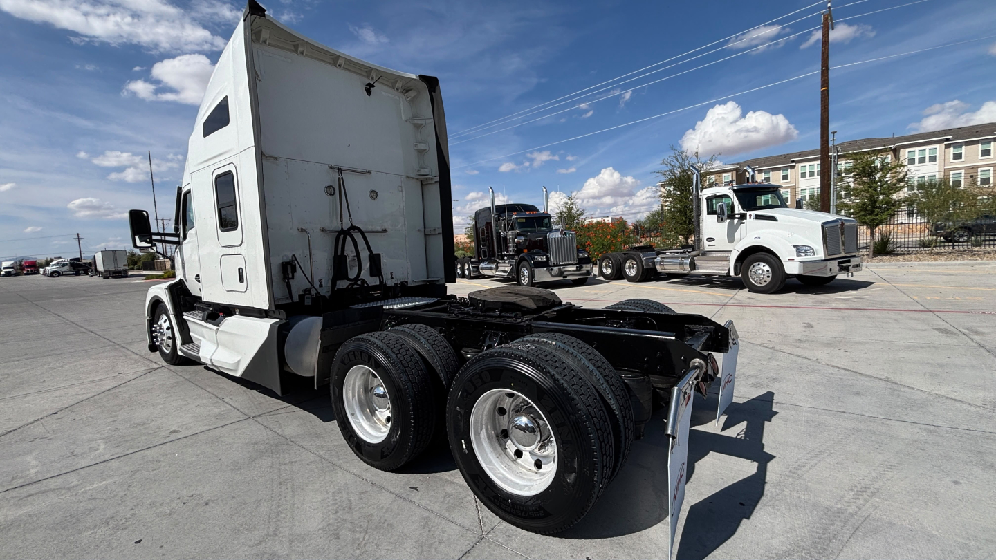Kenworth T680 truck chassis and sleeper cab side view showing dual rear axles and fifth wheel area with white cab and transport yard in background.
