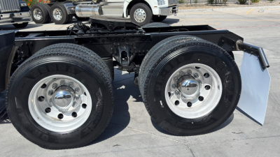 Kenworth T680 chassis view showing tandem rear wheels with chrome hubcaps and dual tires; black frame with mudflaps partially visible.