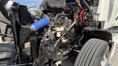 Kenworth T680 engine bay showing intake hoses, wiring, and components in-service; visible coolant reservoir, hoses, and engine block.