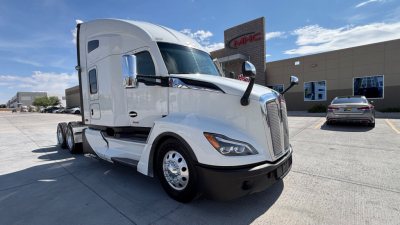Kenworth T680 semi-truck in a dealership lot, front-left angle, chrome mirrors, sleeper cab, white exterior with black bumper.