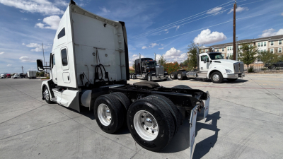 Kenworth T680 truck chassis and sleeper cab side view showing dual rear axles and fifth wheel area with white cab and transport yard in background.