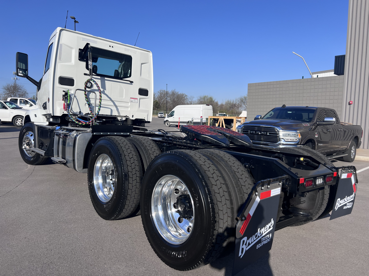 Truck chassis and cab of a 2027 Mack AN64T in a dealership lot, showing dual rear axles and wheel rims.