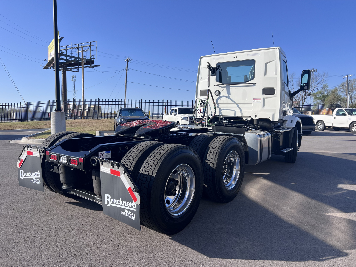 Truck cab from rear three-quarter view showing dual rear axles and fifth-wheel area, chassis, and tires. Clear weather, Mack AN64T truck in a dealership lot.