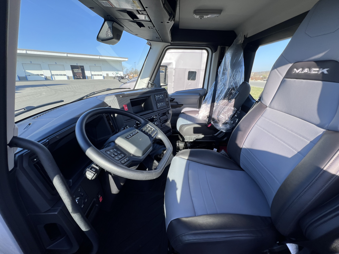 Mack AN64T truck cab interior showing steering wheel, dashboard, and driver seat with protective plastic.